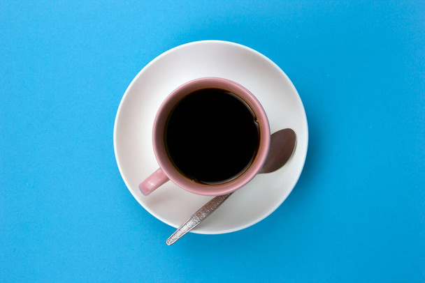 An isolated black coffee on light pink cub on blue background with small spoon - Valokuva, kuva