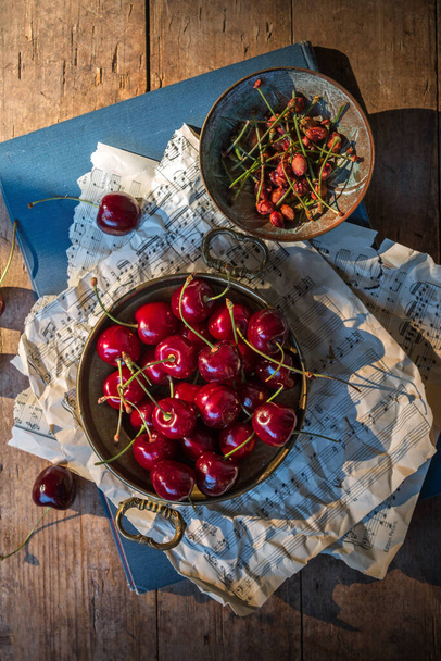 Fresh red cherries and stones in vintage bronze bowls on rustic brown background taken with side lighting - Fotoğraf, Görsel