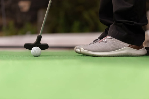 Mini golf - The player prepares to hit the ball with the club. Detail of the ball and the stick - Foto, Imagen