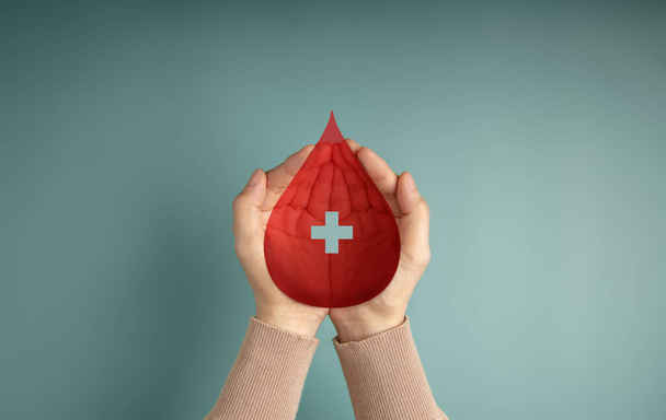 Een bloeddonatie concept. Help, zorg, liefde, ondersteuning. Hand houden van een rode drop en kruis teken. Bovenaanzicht - Foto, afbeelding