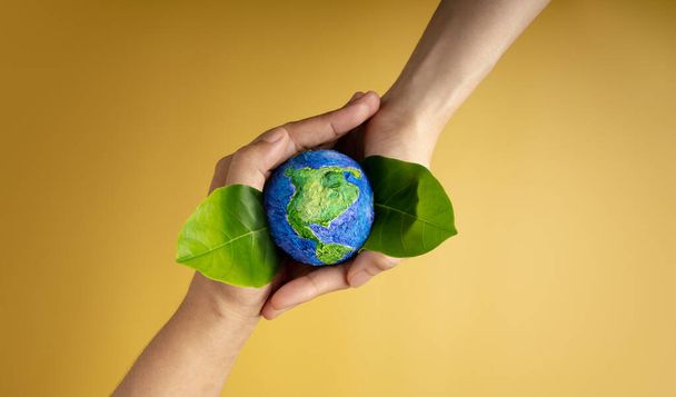 World Earth Day Concept. Green Energy, ESG, Renewable and Sustainable Resources. Environmental and Ecology Care. Hands of People  Embracing Green Leaf and Handmade Globe - Фото, изображение