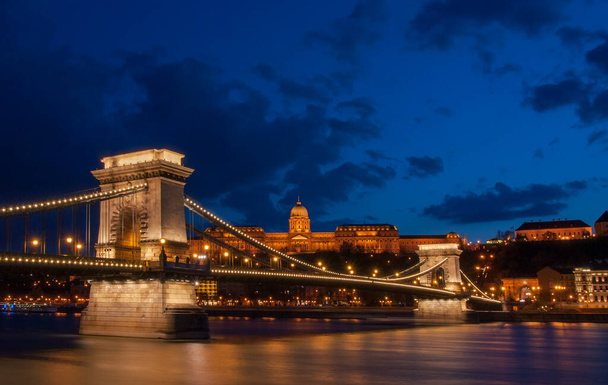 Koninklijk Paleis of het kasteel van Boeda en de beroemde kettingbrug na zonsondergang met verlichting in de danube rivier in Boedapest Hongarije. - Foto, afbeelding