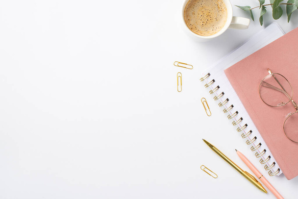 Бизнес-концепция. Фото рабочего места розовые блокноты стаканы чашки кофе зажимы ручки и эвкалипт на изолированном белом фоне с пустым пространством - Фото, изображение