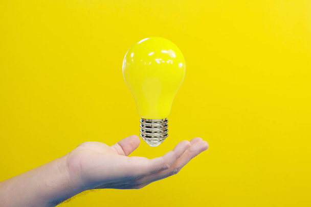 hand holding yellow light bulb on a bright background - Foto, afbeelding