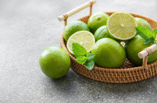 Green  Limes with fresh mint leaves on  wicker tray, concrete background - Foto, imagen