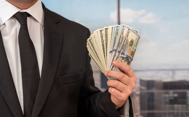 В центральном офисе босс в шикарном костюме берет доллары из собственного кармана. Концепция босса с кучей денег - Фото, изображение