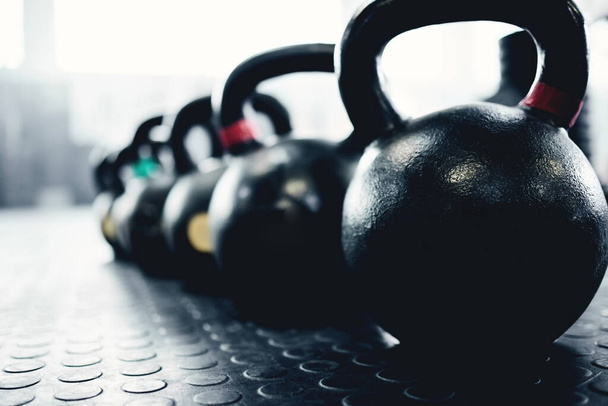 a group of kettlebells on the floor in an empty gym during the day. - Fotografie, Obrázek