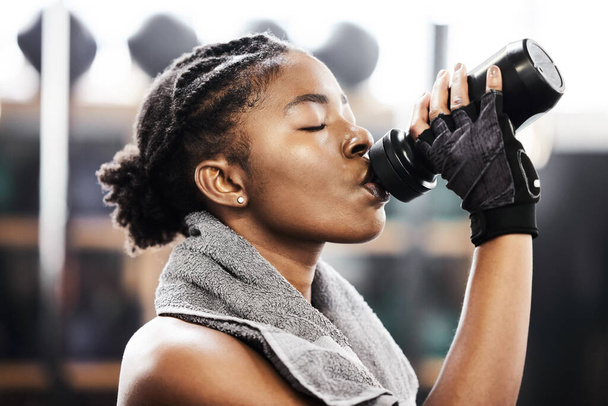 una joven atractiva parada sola en el gimnasio y bebiendo agua después de su entrenamiento. - Foto, imagen