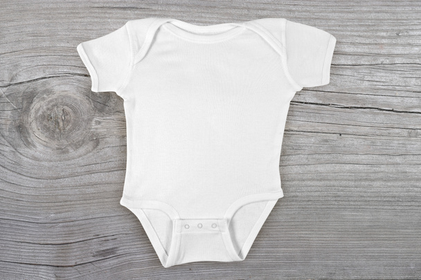 Blank baby onesie lying flat on a weathered gray wooden background. - Foto, Bild