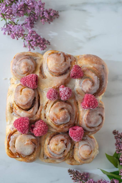 A vertical top shot of freshly baked cinnamon rolls with frozen raspberries - Foto, Imagem