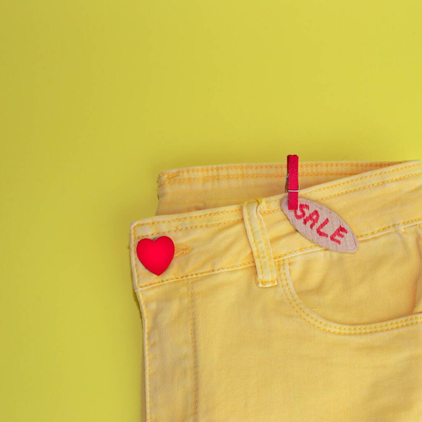 A closeup of yellow jeans with heart button and "sale" tag on a yellow background for copyspace - Φωτογραφία, εικόνα
