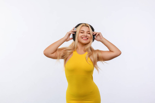 beautiful girl in black headphones and yellow dress listens to music on a white background. different emotions - Photo, Image