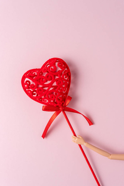 Hand of a doll with red heart on a pink background. Love minimal concept. - Foto, Bild
