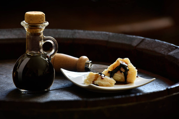 Balsamic Vinegar of Modena with Parmesan flakes set on plates and a wooden barrel  - Foto, Bild