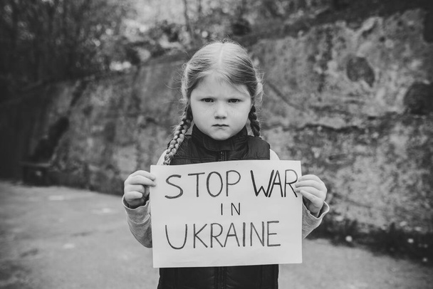 Portrait little upset child calls No War, raises banner with inscription Stop war in Ukraine. Peace, stop russian aggression. United Europe against Russia. Hope for the world. Black and white photo. - Photo, Image