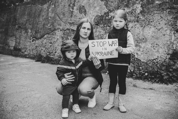 Upset kids with mother protesting war conflict raises banner with inscription message text Stop war in Ukraine. Crisis, peace, stop russian aggression, child against war. No war. Black and white photo - Photo, Image