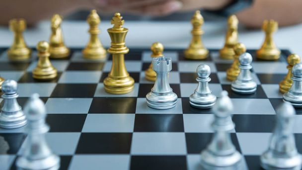 Шахи це настільна гра для поліпшення мислення та планування стратегії. Золоті і срібні шахи на борту в кімнаті для гри. Рука тримає шахи
. - Фото, зображення