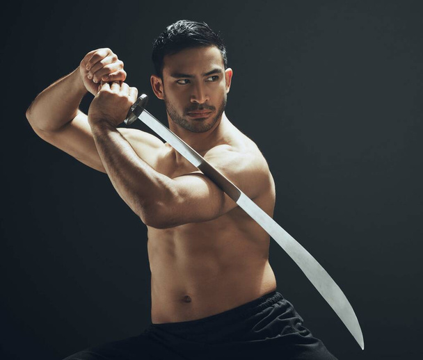 a handsome young man standing alone in the studio and posing with a broadsword. - Foto, imagen