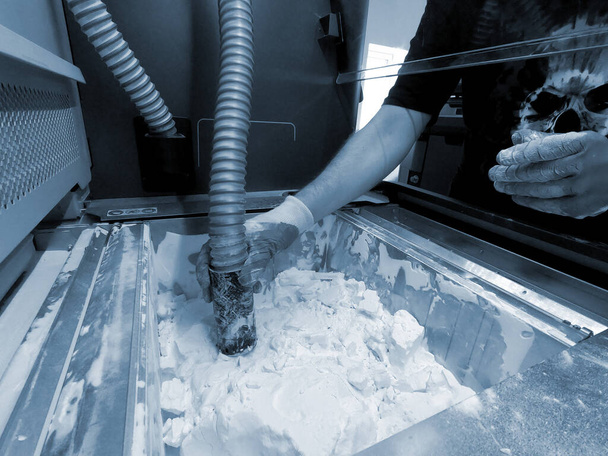 Çalışan bir elektrik süpürgesiyle çalışan bir adam, 3D yazıcının içindeki 3D yazıcıya basılmış bir modeldeki beyaz poliyamit tozunu temizlemek için çalışıyor. Endüstriyel toz 3D yazıcıya basılmış temizleme nesneleri - Fotoğraf, Görsel