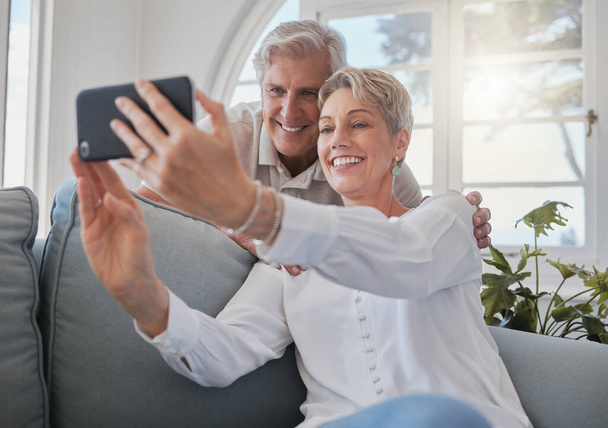 an affectionate senior couple taking selfies while relaxing in the living room at home. - Foto, Imagem