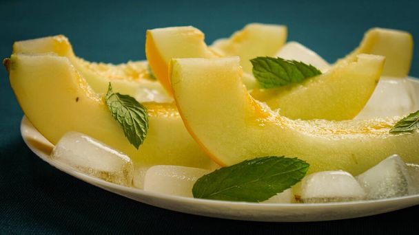 ripe melon with crushed ice and mint leaves, cut into pieces and slices - Foto, afbeelding