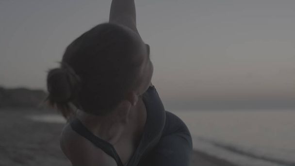 Yoga-Mädchen übt Dreiecksposition am Sandstrand aus nächster Nähe. Sportliche Frau trainiert Beweglichkeit im Stehen am Strand in der Sommerdämmerung. Schlanke Sportlerin macht utthita trikonasana über die Natur.  - Foto, Bild
