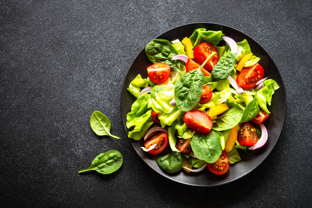 Green salad with fresh vegetables and green leaves at black background. Top view with copy space. - Foto, Imagem