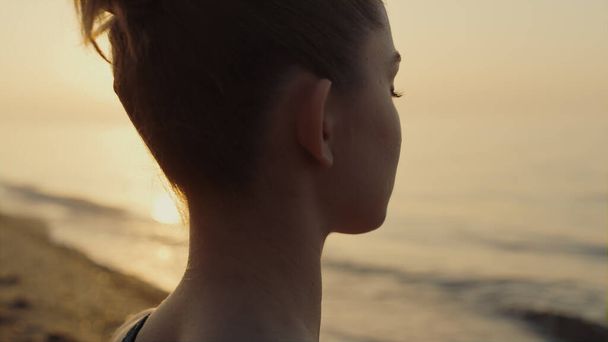 Sportowa kobieta siedząca na pozycji lotosu ćwicząca jogę asana o zachodzie słońca. Zrelaksowana dziewczyna medytująca zamykając oczy na piaszczystej plaży. Młoda atrakcyjna pani czuje spokój harmonii na letniej przyrody. - Zdjęcie, obraz