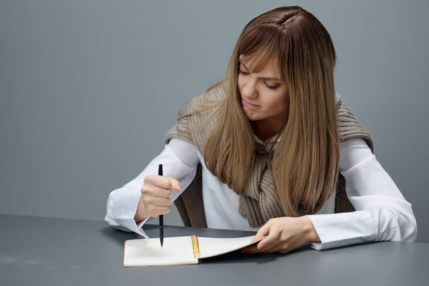 Angry irritated young blonde student lady freelancer in warm sweater hate doing home task at copybook in gray modern home office. Remote Job, Education And Career Profession Concept. Copy space - Photo, Image