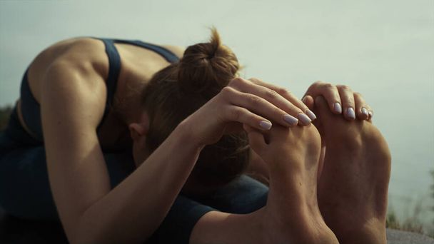 Uvolněná sportovkyně se sehne k nohám sedící jóga pózuje na pláži detailně. Nerozpoznatelná mladá žena, která se protahuje v ranním čase přírody. Flexibilní holka cvičící gymnastiku ve sportovním oblečení. Sport life - Fotografie, Obrázek