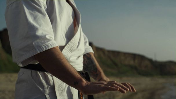 Hands Martial Arts-Meister machen Aufwärmübungen im Stehen am Strand bei Sonnenuntergang aus nächster Nähe. Karate-Kämpfer trainieren Kampftechnik im Freien an Sommerabenden. Sportlicher Mann übt Judo auf Sand am Strand. - Foto, Bild