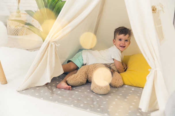 cheerful baby boy posing with his beloved teddy bear in a tent, full shot kids concept. High quality photo - Foto, Bild