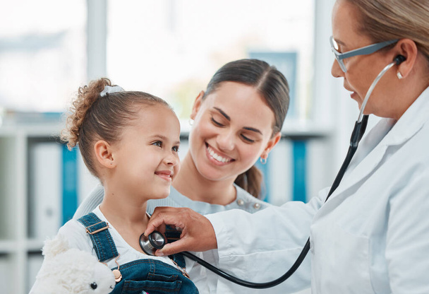 врач осматривает маленькую девочку со стетоскопом в клинике. - Фото, изображение
