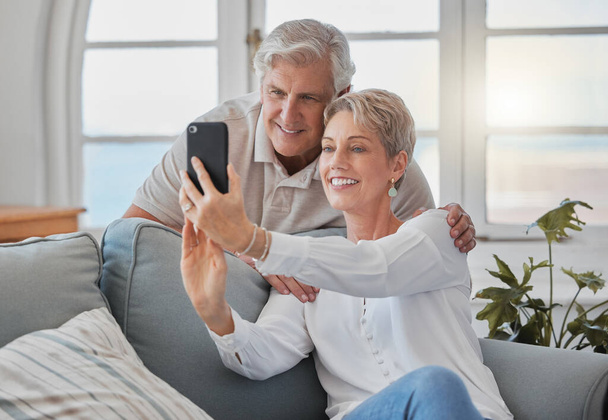 an affectionate senior couple taking selfies while relaxing in the living room at home. - Fotoğraf, Görsel