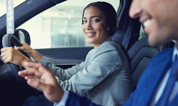 Retrato recortado de una atractiva joven sentada en un coche nuevo mientras hablaba con un apuesto vendedor de coches masculinos sobre un trato. - Foto, imagen