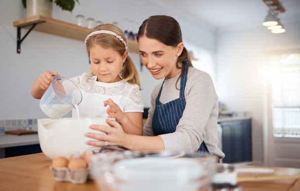 Ένα αξιολάτρευτο κοριτσάκι που βοηθάει τη μητέρα της ενώ μαγειρεύει στο σπίτι.. - Φωτογραφία, εικόνα