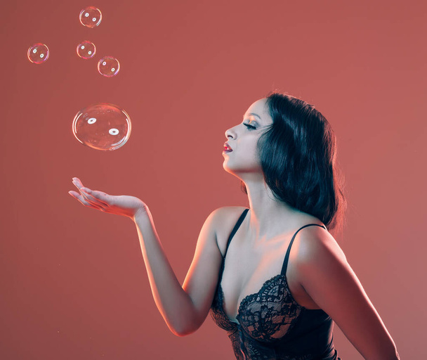 a beautiful young woman posing in studio surrounded by bubbles against a red background. - Valokuva, kuva