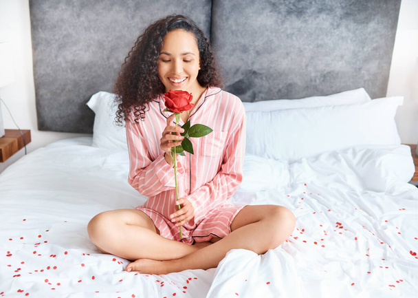 Full length shot of an attractive young woman smelling a rose while sitting cross-legged in her bedroom at home. - Foto, Imagen