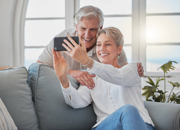 an affectionate senior couple taking selfies while relaxing in the living room at home. - 写真・画像