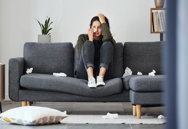 Full length shot of an attractive young woman sitting alone on the sofa at home and crying. - Foto, Bild