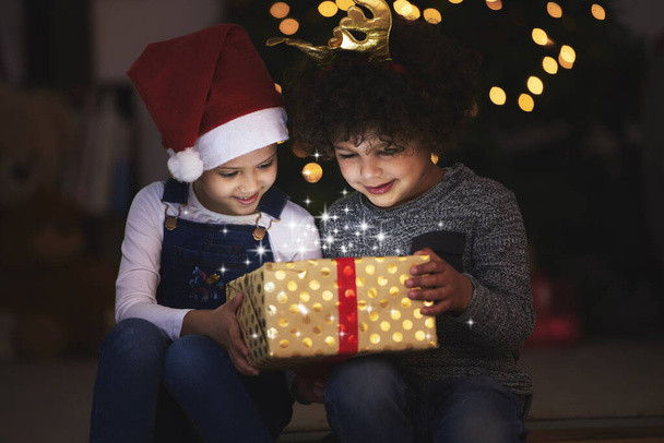 two little siblings opening up a gift together at home. - Foto, afbeelding