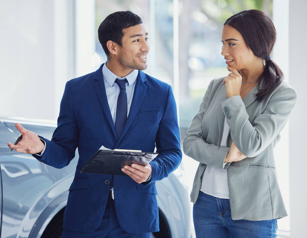 Ένας όμορφος νεαρός πωλητής αυτοκινήτων μιλάει σε μια πελάτισσα στο πάτωμα της έκθεσης.. - Φωτογραφία, εικόνα