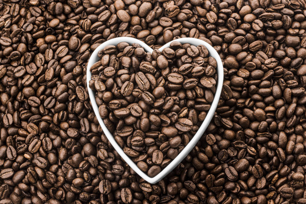 Coffee Beans in White Heart Shape Plate on Fresh Coffee Beans Background. Flat Lay. High quality photo - Photo, Image