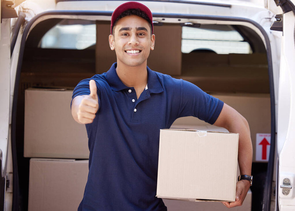 Retrato de un joven repartidor mostrando los pulgares hacia arriba mientras carga cajas de una furgoneta. - Foto, Imagen