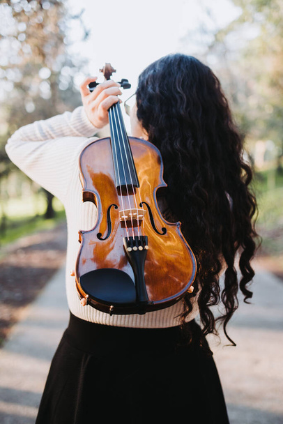 brunette woman holding a violin on her back, walking through the park road at sunset. High quality photo - Foto, Imagem