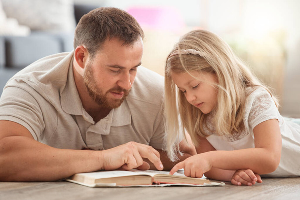 un jeune père et sa fille lisant un livre ensemble à la maison. - Photo, image