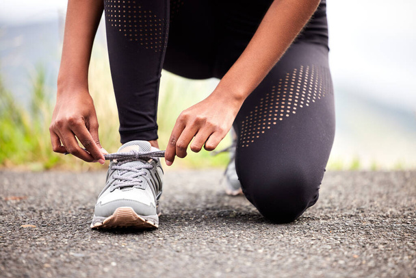Closeup shot of an unrecognizable woman tying her shoelaces while exercising outdoors. - Foto, imagen