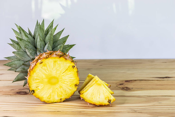 halbierte und in Scheiben geschnittene Ananas auf einem Holztisch in der Nähe süße und saure Früchte nahrhaft und reich an Vitaminen - Foto, Bild