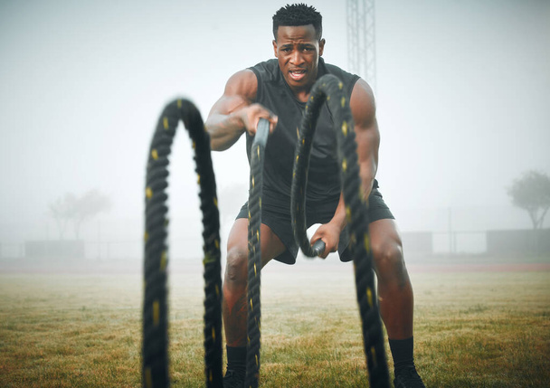 Portrait of a muscular young man exercising with battle ropes outdoors. - Foto, imagen