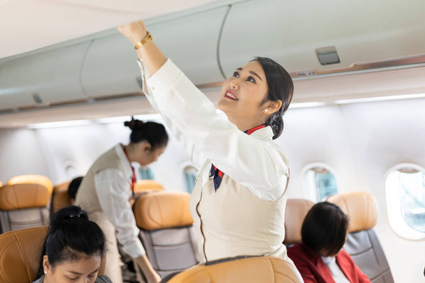 Asian female flight attendant closing overhead luggage compartment lid for carry on baggage after passengers are seated and prepare to take off - Photo, image